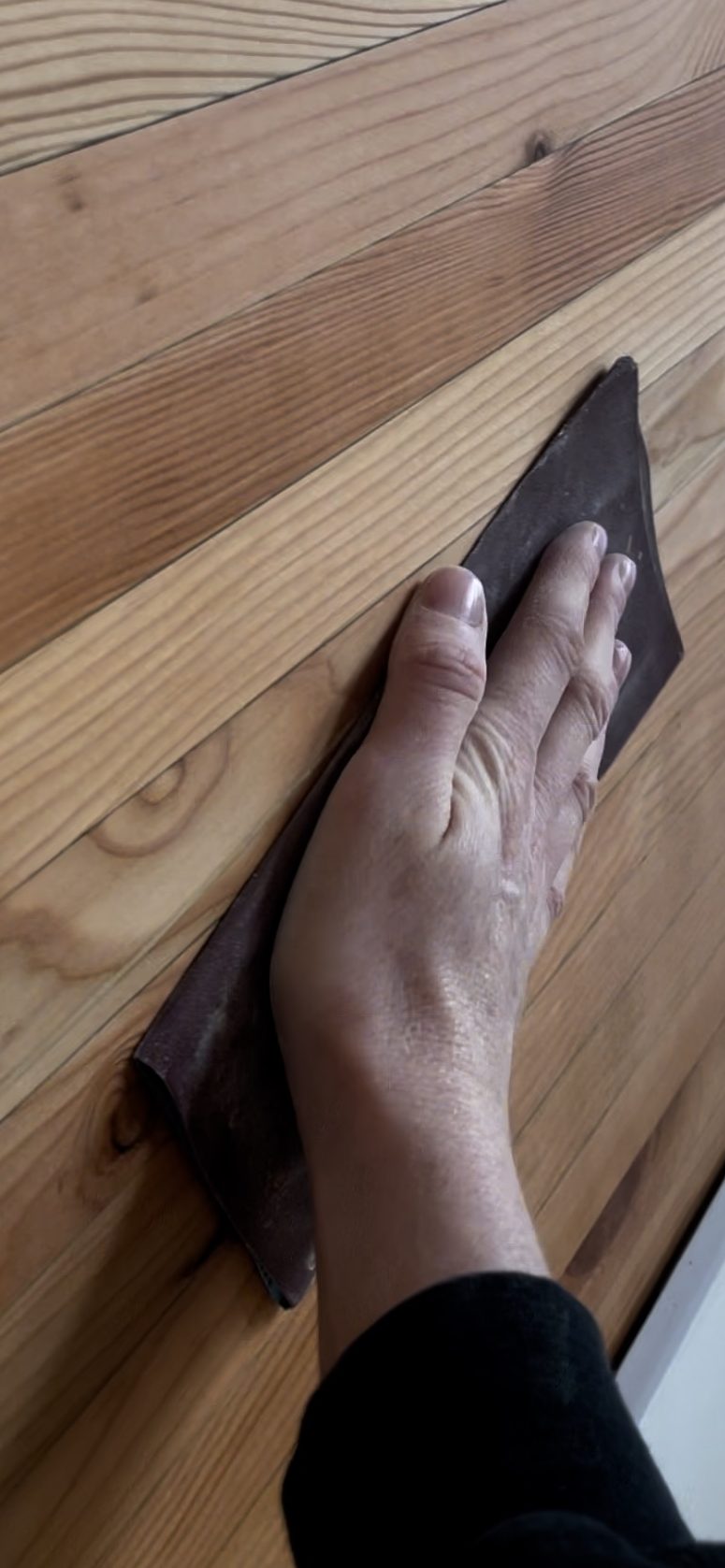 A close-up image of a hand sanding a wooden surface, emphasizing the textured grain of the wood.